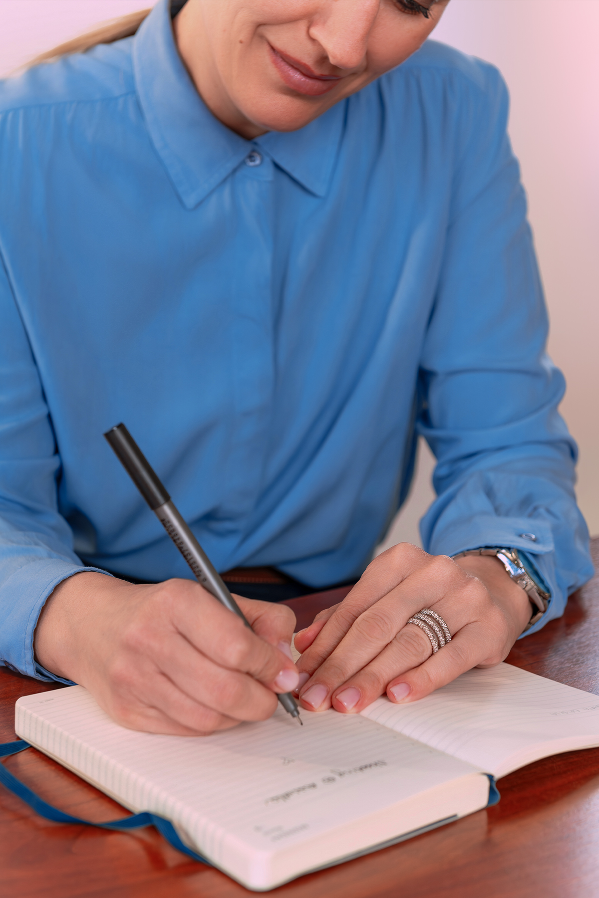 Imprenditrice in camicia azzurra che scrive su un quaderno, parete rosa