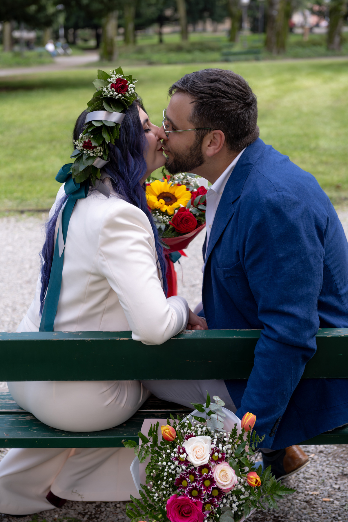 Coppia di sposi su una panchina verde con il bouquet