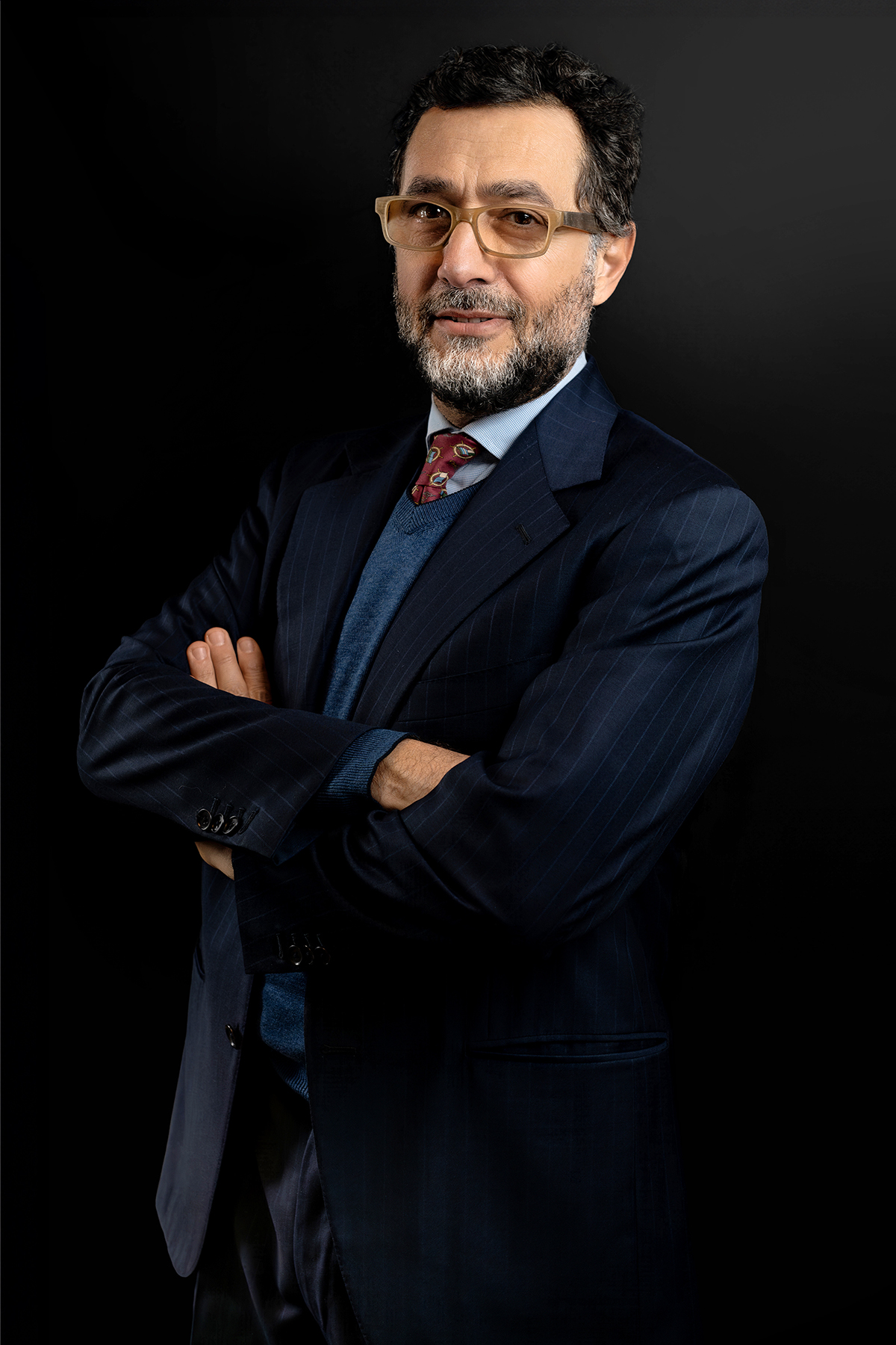 Ritratto di uomo con occhiali e barba, abito blu su fondo nero